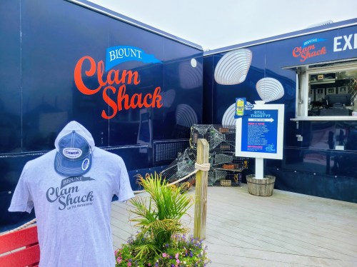 A food truck named "Biont Clam Shack" with a t-shirt display and a menu sign, surrounded by plants and decor.