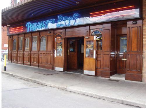 Exterior of Primanti Bros. restaurant featuring wooden doors and neon signage, with a welcoming entrance.