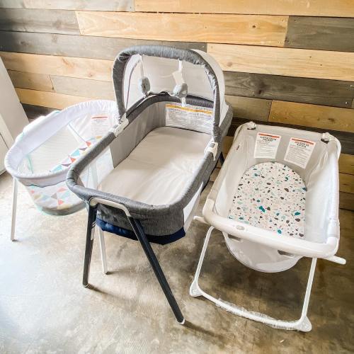 Three baby bassinets in a room with wooden walls, featuring different designs and colors.