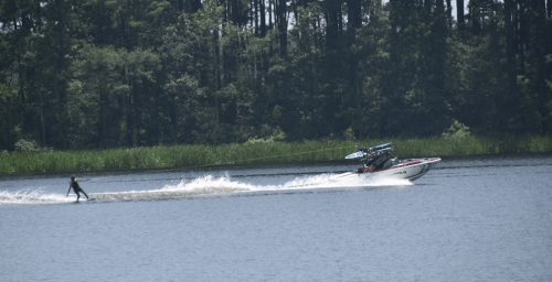 A person water skiing behind a boat on a calm lake, surrounded by lush greenery.