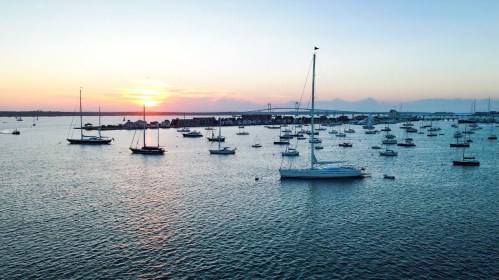 A serene sunset over a harbor filled with sailboats, casting reflections on the calm water.