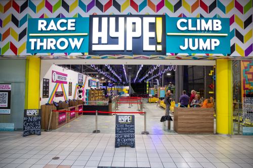 Entrance to HYPE! amusement center featuring colorful signage and various activity areas for racing, throwing, climbing, and jumping.