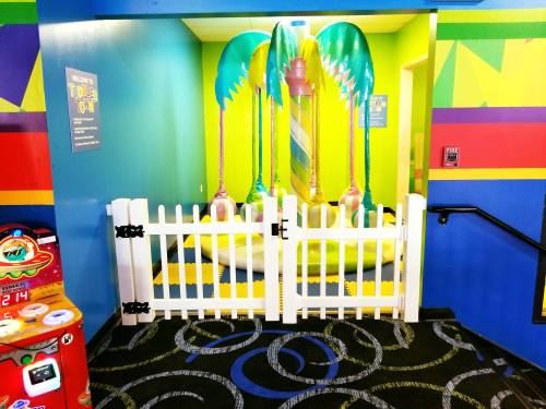 Colorful play area with palm tree decorations, a white picket fence, and a vibrant wall design. Arcade game nearby.