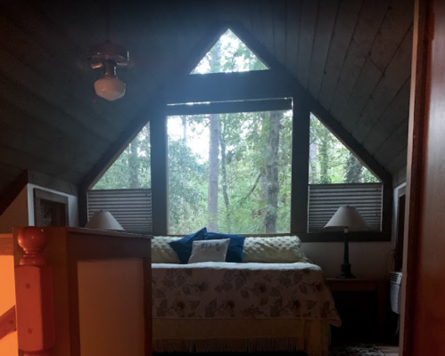 Cozy bedroom with a sloped ceiling, large windows overlooking a forest, and a bed adorned with decorative pillows.