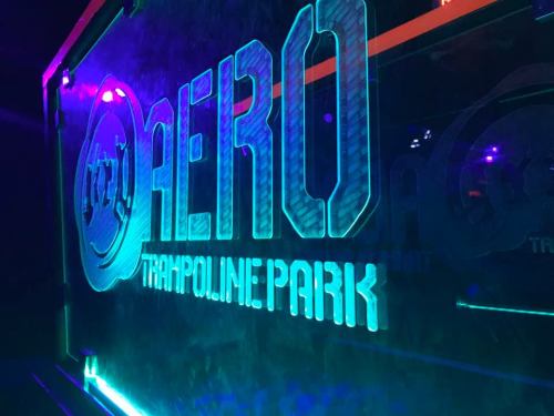 Neon sign of "AERO TRAMPOLINE PARK" illuminated in blue and purple lights.