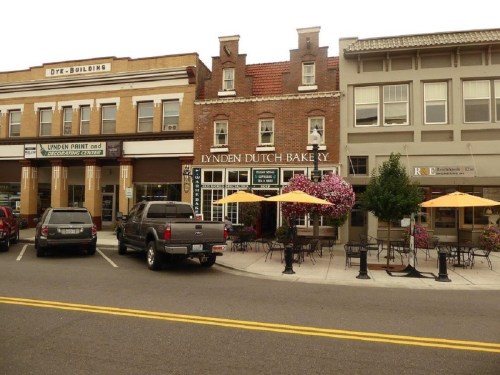 A charming street scene featuring the Lynden Dutch Bakery and nearby shops, with outdoor seating and colorful flowers.