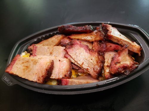 A black takeout container filled with sliced smoked brisket, showcasing a variety of charred and tender meat pieces.