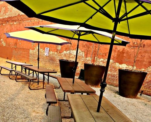 Outdoor seating area with wooden tables and large umbrellas against a textured brick wall.