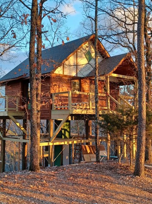 A wooden treehouse with a porch, surrounded by trees and bathed in warm sunlight during sunset.