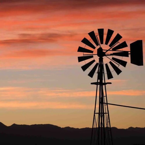 A silhouette of a windmill against a colorful sunset sky with mountains in the background.