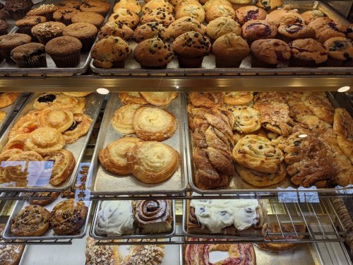 A display case filled with various baked goods, including muffins, pastries, and cinnamon rolls.