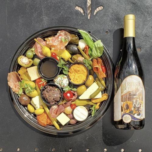 A gourmet charcuterie board with meats, cheeses, olives, and dips, alongside a bottle of Creekside Cellars Rosso wine.