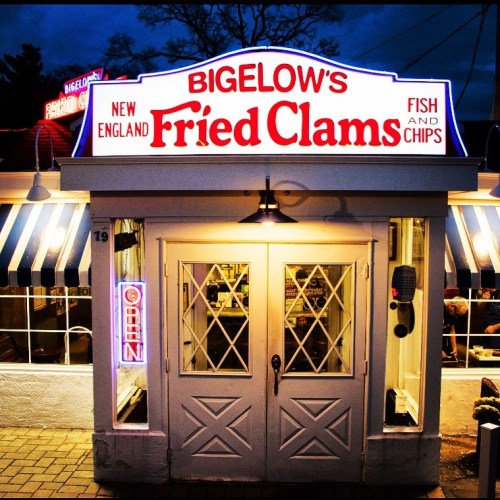 A brightly lit restaurant entrance with a sign reading "Bigelow's Fried Clams" and "Open" in neon lights.