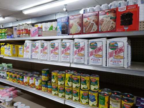 A grocery store shelf displaying various food items, including flour bags and canned goods.