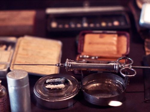 A vintage syringe and medical tools displayed on a table, surrounded by various containers and instruments.