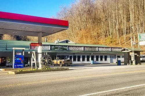 A gas station and a rustic building with a sign for Old Springs Park, surrounded by wooded hills.