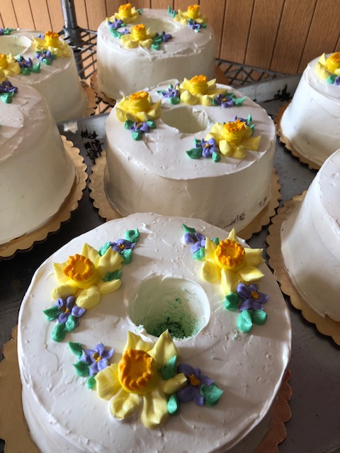 A display of decorated cakes with white frosting and colorful floral designs on top.