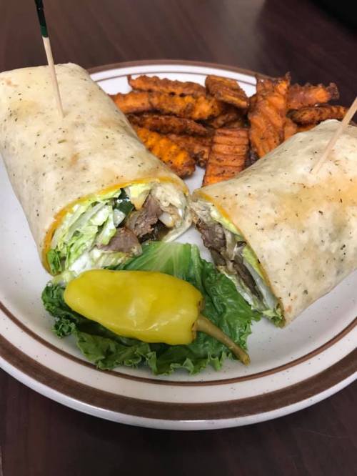A plate with a cut wrap filled with lettuce and meat, accompanied by sweet potato fries and a pepper.
