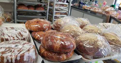 A display of various baked goods, including glazed pastries and loaves, wrapped in plastic on trays.