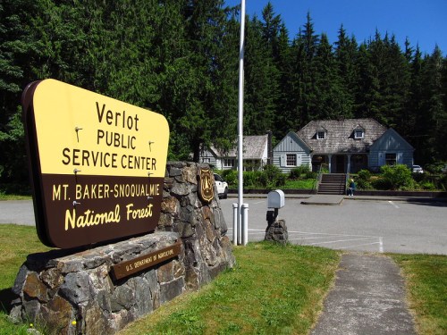 Sign for Verlot Public Service Center in Mt. Baker-Snoqualmie National Forest, with a building and trees in the background.