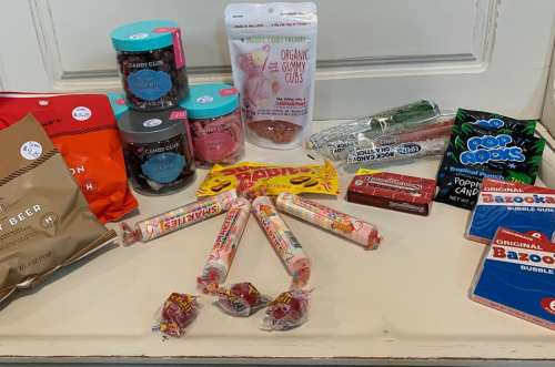 A variety of candies and snacks displayed on a table, including gummies, lollipops, popcorn, and chocolate treats.