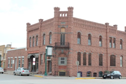 Historic red stone building with castle-like features, large windows, and a corner location in a small town.