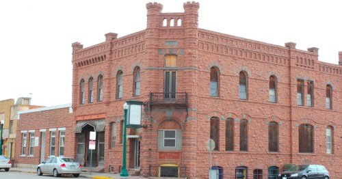Historic red stone building with decorative features, large windows, and a balcony, located on a street corner.