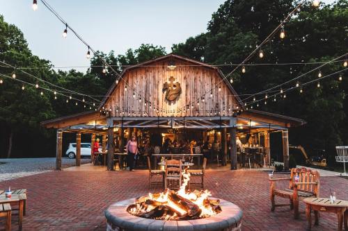 A rustic barn with string lights, a fire pit in front, and people socializing outdoors in a cozy setting.