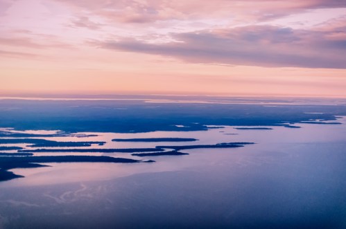 Aerial view of serene water with islands at sunset, featuring soft pink and purple hues in the sky.