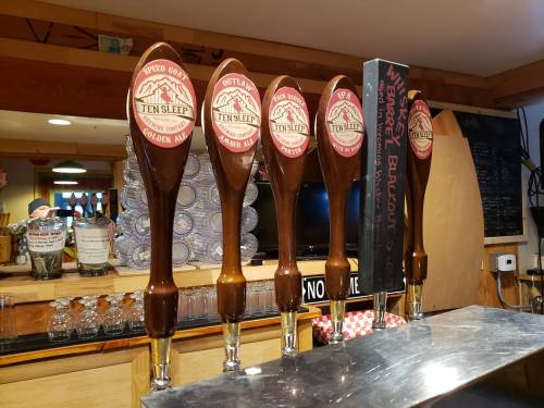A row of wooden beer taps with labels for Ten Sleep Brewing Co. and Outlaw Brewing, set against a bar backdrop.