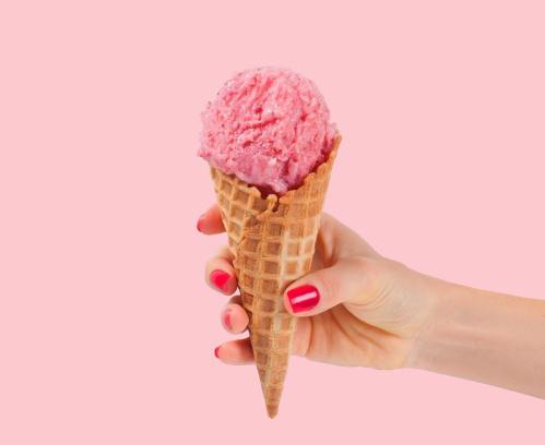 A hand holding a waffle cone filled with pink ice cream against a pink background.