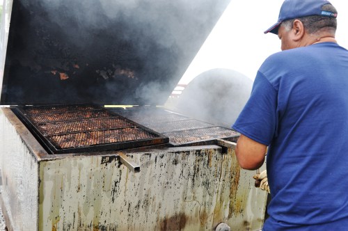 A person cooking on a large grill, with smoke rising from the food as the lid is lifted.