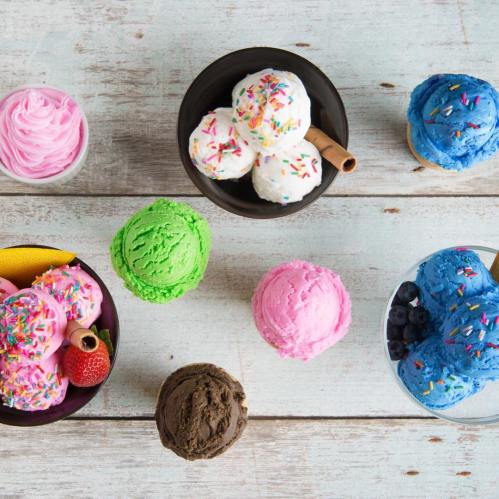 A colorful assortment of ice cream scoops in bowls, featuring pink, green, blue, and chocolate flavors with sprinkles.