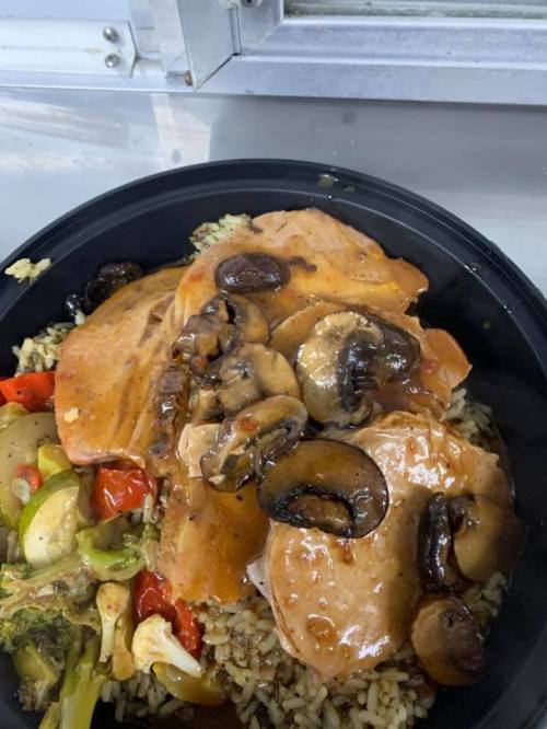 A black bowl filled with rice, sliced turkey, mushrooms, and mixed vegetables in a savory sauce.