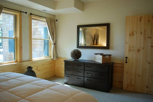 Cozy bedroom with wooden accents, a dresser, mirror, and natural light from two windows.