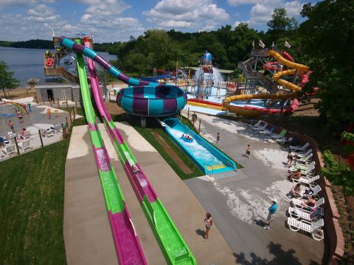 Aerial view of a water park featuring colorful slides, a lazy river, and people enjoying the sun by the pool.