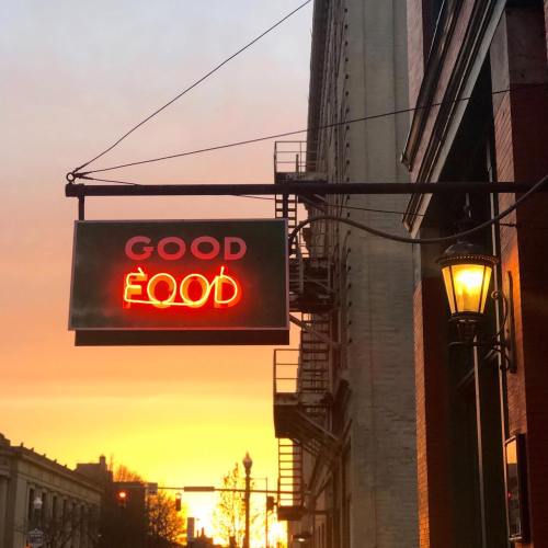 Neon sign reading "GOOD FOOD" against a sunset backdrop, with a streetlamp nearby.