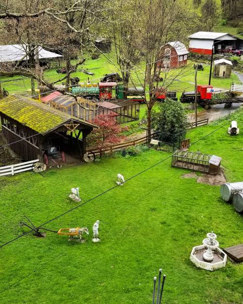 A scenic view of a farm with green grass, barns, and a train passing through the landscape. Statues and structures are visible.