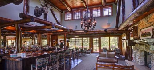 Cozy lodge interior featuring a wooden bar, rustic decor, large windows, and a stone fireplace.