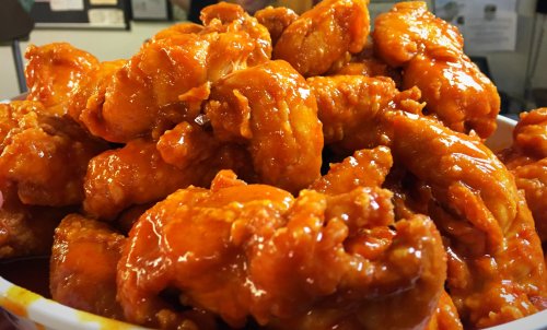 A close-up of a bowl filled with crispy, orange-glazed chicken wings.