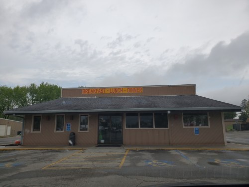 A one-story restaurant building with a sign that reads "Breakfast - Lunch - Dinner" under a cloudy sky.