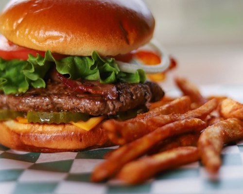 A close-up of a juicy burger with lettuce, tomato, pickles, and cheese, served with crispy fries on the side.