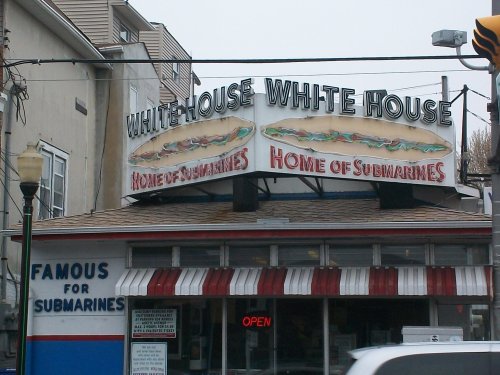 Sign for "White House" restaurant featuring "Home of Submarines" and "Famous for Submarines" in a casual setting.