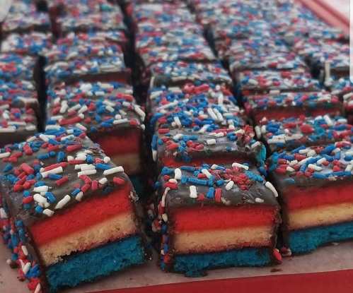 Colorful layered dessert squares with red, white, and blue frosting, topped with sprinkles, arranged neatly in rows.