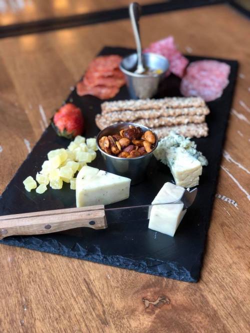 A charcuterie board featuring cheeses, meats, nuts, fruit, and pretzel sticks on a slate platter.