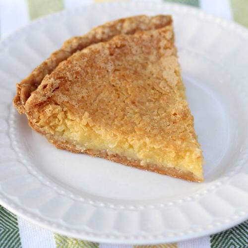 A slice of coconut pie on a white plate, featuring a golden, flaky crust and a textured, creamy filling.