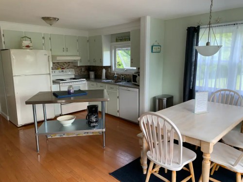Bright kitchen with white cabinets, a dining table, and a coffee maker, featuring wooden floors and large windows.