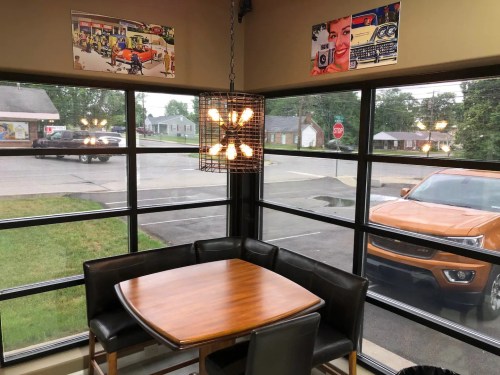 A cozy dining area with a wooden table, black chairs, and large windows showcasing street views and colorful wall art.