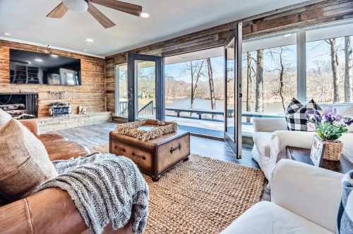 Cozy living room with a lake view, featuring a brown leather sofa, a coffee table, and large glass doors.