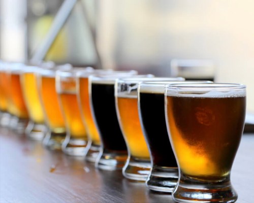 A row of various beer glasses, showcasing different colors and styles, on a wooden table.